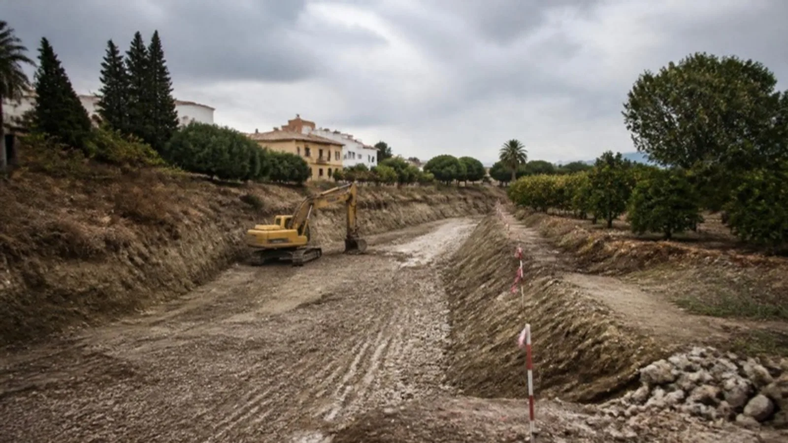 Cauce seco de un barranco cerca de Valencia con márgenes erosionados, una excavadora y estacas de replanteo