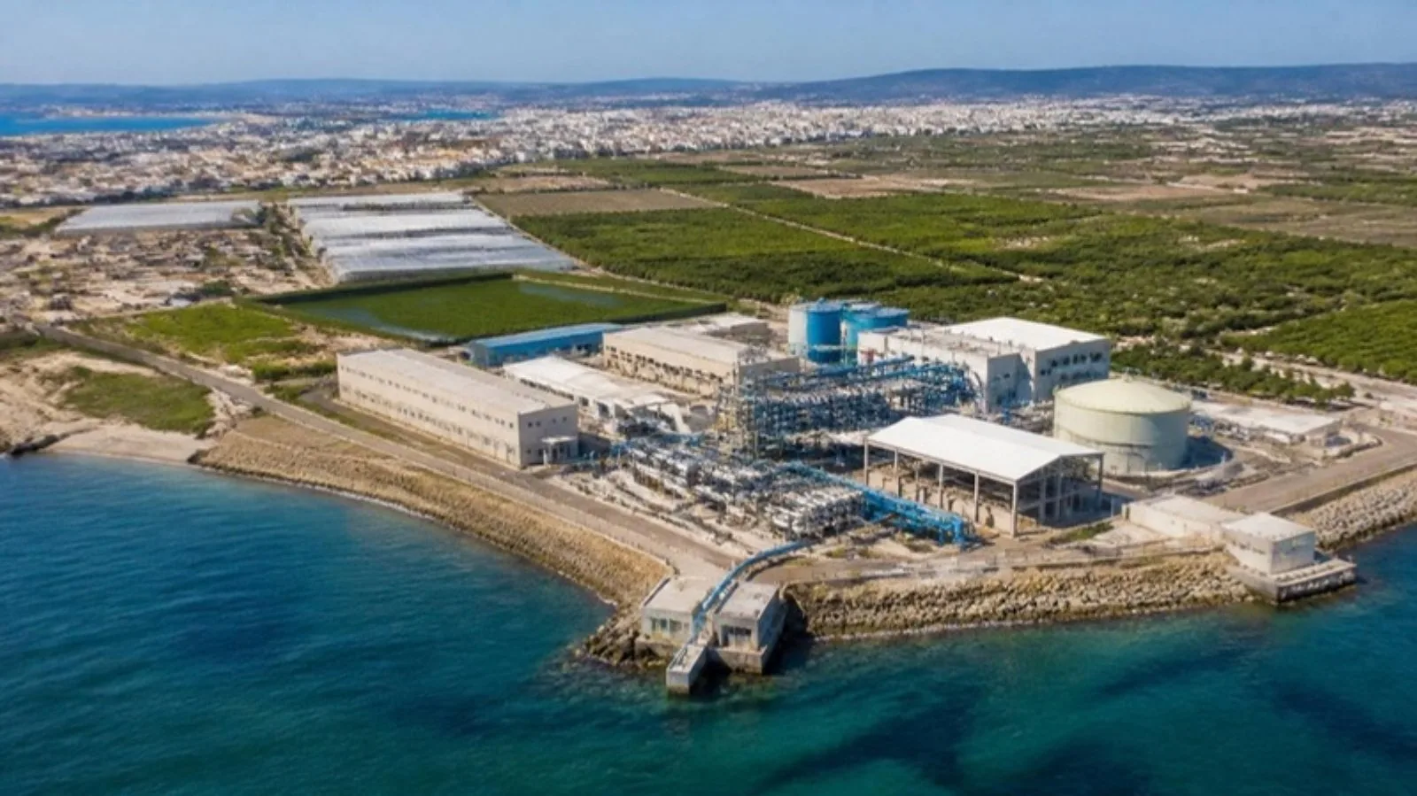 Planta desaladora junto al Mediterráneo con huertos de regadío e invernaderos detrás
